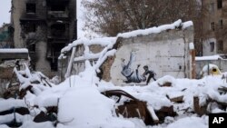 Sebuah karya seni yang dibuat oleh seniman jalanan Inggris Banksy terlihat di sebuah bangunan yang dihancurkan oleh tentara Rusia, di antara puing-puing yang tertutup salju di Borodyanka, wilayah Kyiv, Ukraina, Selasa, 6 Desember 2022. (AP/Efrem Lukatsky)