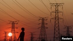 FILE - A local walks past electricity pylons during frequent power outages from South African utility Eskom, caused by its aging coal-fired plants, in Orlando, Soweto, South Africa, Sept. 28, 2022.