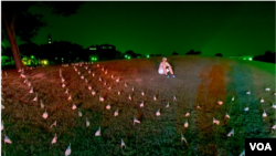 Seorang aktivis duduk di antara bendera yang ditempatkan di dekat Monumen Washington untuk mengenang 180.000 orang yang telah meninggal akibat pandemi Covid-19 di AS, Washington, Agustus 2020. (Foto: VOA)
