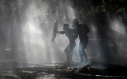 Anti-government demonstrators shield themselves amid the spray of a police water cannon trying to disperse them in Santiago, Chile, Friday, Dec. 27, 2019.