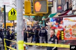 Polisi New York (NYPD) berkumpul di pintu masuk halte kereta bawah tanah di wilayah Brooklyn, New York, Selasa, 12 April 2022. Lima orang ditembak pria tak dikenal di sebuah stasiun kereta bawah tanah di Brooklyn, New York. (AP/John Minchillo)