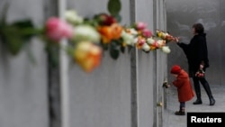 2014年11月9日，德国柏林举行柏林墙倒塌25周年纪念仪式。图为一对母女把玫瑰花放在在柏林墙上。