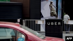 A taxi passes by an Uber station outside a shopping mall in Beijing on August 1, 2016. Ride-sharing giant Uber is to merge its China operations with local rival Didi Chuxing, reports said on August 1, ending a ferocious battle for market share in the world's second-largest economy.