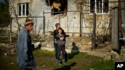 A family stands next to their heavily damaged house in Shandrygolovo village, near Lyman, Ukraine, Oct. 4, 2022.