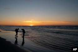 The sun sets in the horizon as Ned Ahgupuk and his girlfriend, Kelsi Rock, piggybacking their 1-year-old son, Steven, stroll along the beach on the Arctic Ocean in Shishmaref, Alaska, Friday, Sept. 30, 2022.