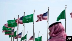 FILE - A man stands under U.S. and Saudi Arabian flags prior to a visit by President Joe Biden, at a square in Jeddah, Saudi Arabia, July 14, 2022. 