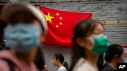 People walk past a Chinese flag on a tourist shopping street on the first day of the National Day holiday period in Beijing, Oct. 1, 2022. 