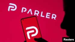 FILE - A woman is seen holding smartphone with Parler logo in front of displayed same logo in this illustration taken May 17, 2021. 