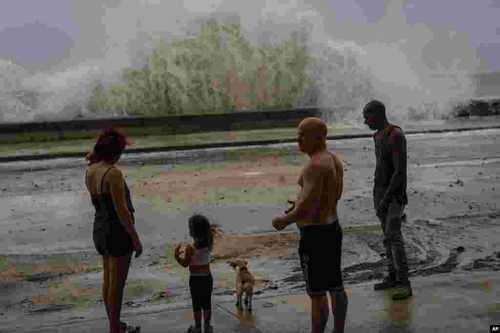 People stand along a waterfront as huge waves crash against a seawall in the wake of Hurricane Ian in Havana, Cuba, Sept. 28, 2022. 