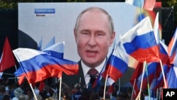 People watch on a large screen, as Russian President Vladimir Putin delivers his speech after a ceremony to sign the treaties for four regions of Ukraine to join Russia in Moscow's Kremlin, during a meeting in Sevastopol, Crimea, Friday, Sept. 30, 2022. (AP Photo)