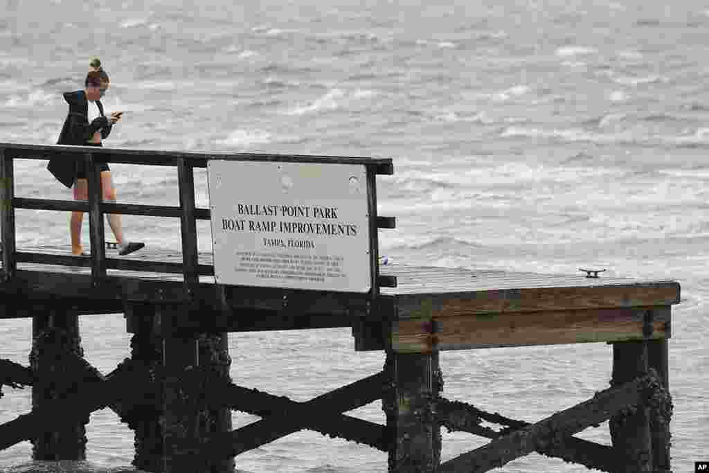 A woman looks at her phone on the Ballast Point Pier on Tampa Bay ahead of Hurricane Ian, Sept. 28, 2022, in Tampa, Florida. 
