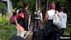 FILE - A Royal Canadian Mounted Police (RCMP) officer watches as a family from Haiti arrive to cross the U.S.-Canada border into Canada from Roxham Road in Champlain, New York, August 11, 2017.