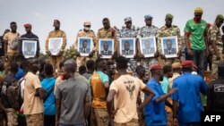 Mourners hold photos of some of the 27 soldiers killed as they escorted 207 vehicles in a convoy during their funeral at the General Sangoule Lamizana military camp in Ouagadougou, Burkina Faso, Oct. 8, 2022.