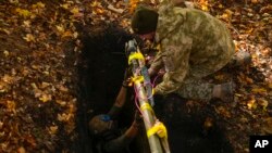 Ukrainian territorial defense deminers put Russian weapons and ammunition in a hole to be destroyed as they clear mines near Hrakove village, Ukraine, Oct. 13, 2022.