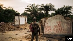 Un membre des forces armées congolaises se tient à côté d'un bâtiment incendié dans la ville occidentale de Yumbi, à Maï-Ndombe, RDC, 1er février 2019.