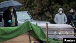 지난 9일 뉴욕 브루클린의 묘지 앞에서 마스크를 착용한 시민이 신종 코로나바이러스 감염증(COVID-19) 사망자 시신이 안치된 관 앞에 서 있다. 