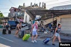 Foreign tourists pull their suitcases as they walk past damaged buildings following a strong earthquake in Pemenang, North Lombok, Indonesia, Aug. 6, 2018.