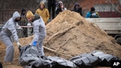 FILE - Men wearing protective gear exhume bodies of some of the civilians killed during the Russian occupation of Bucha, on the outskirts of Kyiv, Ukraine, April 13, 2022.