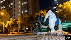 Deliverymen wearing protective suits carry bags of food at the gate of a residential community in Shanghai, April 11, 2022. 