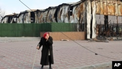 An elderly local resident stands behind a destroyed part of the Illich Iron & Steel Works Metallurgical Plant, the second largest metallurgical enterprise in Ukraine, in an area controlled by Russian-backed separatist forces in Mariupol, Ukraine, April 16, 2022.