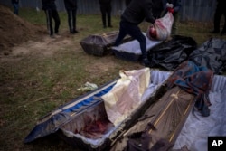 Volunteers transfer into a bag the body of a civilian killed by Russian soldiers, after its removal from a mass grave, during an exhumation in Mykulychi, Ukraine, April 17, 2022.