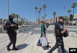 Anggota polisi perbatasan Israel mengawal seorang perempuan Israel di dekat Gerbang Damaskus di Kota Tua Yerusalem, di tengah langkah-langkah keamanan yang meningkat, 15 April 2022. Lebih dari 100 orang terluka dalam kekerasan baru, yang terjadi setelah tiga minggu ketegangan akibat kekerasan di Israel dan Tepi Barat bersamaan dengan perayaan Passover warga Yahudi, Paskah umat Kristiani dan bulan suci Ramadan umat Muslim. (Foto: GIL COHEN-MAGEN / AFP)