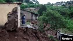 Une femme se tient à sa porte d'entrée après que de fortes pluies ont causé des dégâts d'inondation à KwaNdengezi, Durban, Afrique du Sud.