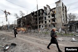 People walk past a residential building, which was heavily damaged in the southern port city of Mariupol, Ukraine during Russia's invasion of Ukraine, April 18, 2022.