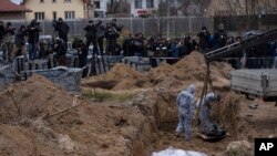 Para petugas menunjukkan warga sipil yang menjadi korban tewas di kuburan massal di Bucha, Ukraina kepada Penuntut ICC dan media, hari Rabu (14/4).