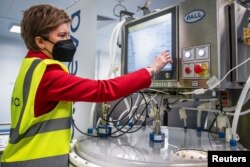 Menteri Pertama Skotlandia, Nicola Sturgeon mengoperasikan bioreaktor ekspansi sel saat meninjau pabrik vaksin Valneva Scotland yang baru di Livingston, Skotlandia, Inggris 28 Maret 2022. (Andy Buchanan/Pool via REUTERS)