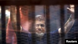 Former Egyptian President Mohamed Mursi waves as he enters for his trial with other Muslim Brotherhood members at a court in the outskirts of Cairo, May 16, 2015. 