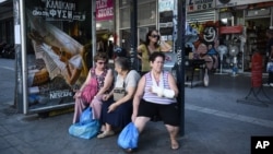 FILE - Elderly women wait at a bus stop in central Athens, Aug. 13, 2015.