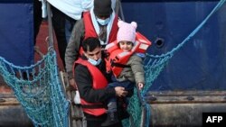 A young child is carried as migrants are helped to disembark at the port of Dover after being picked up crossing the English Channel from France, April 14, 2022, at Dover.