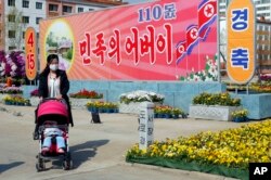 Seorang perempuan mendorong bayi dengan kereta dorong di depan poster bertuliskan "Bapak Bangsa", menandai peringatan 110 tahun mendiang pemimpin Korea Utara Kim Il-sung, di Pyongyang, DPRK, pada Jumat, 15 April 2022. (AP/Jon Chol Jin)