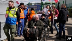 Volunteers help refugees in a wheelchair after fleeing the war from neighboring Ukraine at the border crossing in Medyka, southeastern Poland, April 11, 2022.