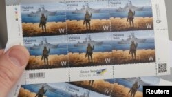 Čovek drži poštansku marku na kojoj je prikazan ukrajinski vojnik i nedavno uništen ruski ratni brod "Moskva", u sedištu ukrajinske pošte u Kijevu, 14. aprila 2022.