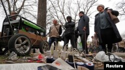 Warga lokal tampak menunggu barang-barang elektronik milik mereka yang tengah dicas dengan generator di sebuah pasar di Mariupol, Ukraina, pada 19 April 2022. (Foto: Reuters/Alexander Ermochenko)