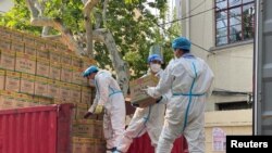 Petugas mengenakan APD menurunkan kotak berlabel kecap dari truk, di tengah wabah COVID-19 di Shanghai, China 21 April 2022. (REUTERS/Andrew Galbraith)