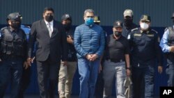 Former Honduran President Juan Orlando Hernandez, center, is taken in handcuffs to a waiting aircraft as he is extradited to the United States, at an Air Force base in Tegucigalpa, Honduras, April 21, 2022.