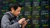 A man uses smartphone in front of an electronic stock indicator of a securities firm in Tokyo, March 26, 2018.