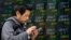 A man uses smartphone in front of an electronic stock indicator of a securities firm in Tokyo, March 26, 2018.