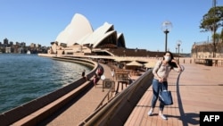 FILE - A lone tourist poses for a photo in Circular Quay in Sydney on March 20, 2020, after Australia moved to seal off its borders the day before, announcing unprecedented bans on entry for non-residents.