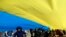 Children play as people hold up a giant Ukrainian flag to protest against the Russian intervention in Ukraine during the celebration of Lithuania's independence in Vilnius, Lithuania, Tuesday March 11, 2014.