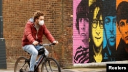 Seorang pria mengenakan masker bersepeda melewati mural band "The Beatles" di tengah pandemi virus corona, Liverpool, Inggris, 13 Oktober 2020. 