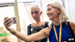 یکی از شرکت‌کنندگان در جلسه «ای‌آی فور گودز» با سوفیا، ربات انسنان‌نما، سلفی می‌گیرد - ۱۴ تیر ۱۴۰۲