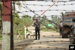 FILE - A Myanmar police officer stands watch as journalists arrive in the village of Shwe Zar, in the northern part of Rakhine state, Sept. 6, 2017.