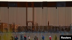 Migrants seeking asylum gather near the border wall after crossing a razor wire fence deployed to inhibit their crossing into the United States, as a member of the Texas National Guard escorts them, as seen from Ciudad Juarez, Mexico,Dec. 19, 2024. 
