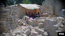 A family uses tarps taken from a refugee camp to get shelter from the sun, with bricks for rebuilding their homes all around them in the PK5 neighborhood of Bangui, Feb. 2017. (Z. Baddorf/VOA)