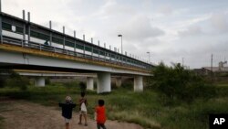 FILE - Migrant children walk with their families along the Rio Grande, as pedestrian commuters use the Puerta Mexico bridge to enter Brownsville, Texas, seen from Matamoros, Tamaulipas state, Mexico, June 26, 2019.