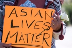 A demonstrator holding a sign and a flower takes part in a rally to raise awareness of anti-Asian violence, near Chinatown in Los Angeles on Feb 20, 2021.